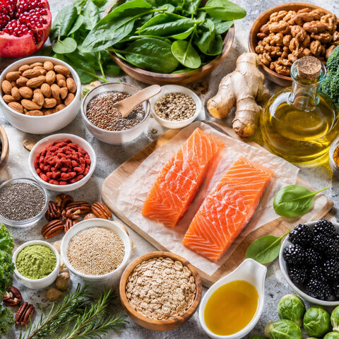An overhead spread of anti-inflammatory whole foods — wild salmon, blueberries, leafy greens, nuts, seeds, avocado, turmeric, ginger, and olive oil.