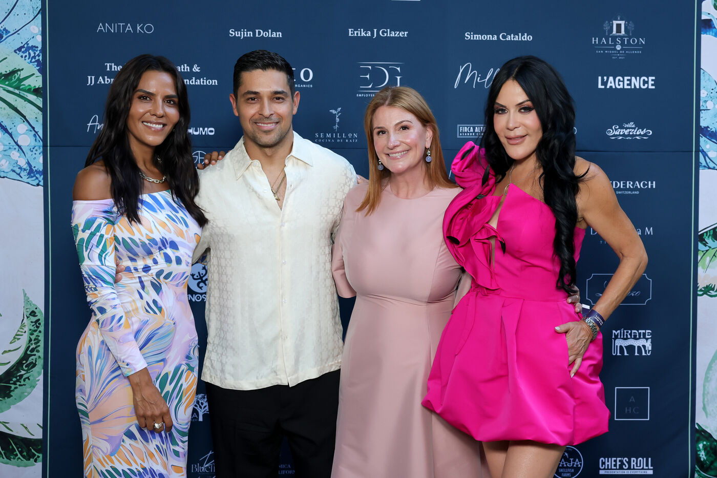 Elsa Marie Collins in a pastel printed dress, honoree Wilmer Valderrama in a cream shirt, and Zoe Winkler Reinis in a blush dress with a fourth guest in fuchsia, photographed against the Soir&eacute;e step-and-repeat.