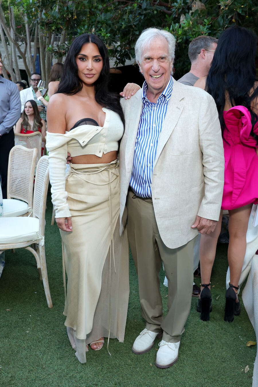 Kim Kardashian in a cream cardigan and skirt stands with Henry Winkler in a cream linen jacket and blue striped shirt on the lawn at the Soir&eacute;e.
