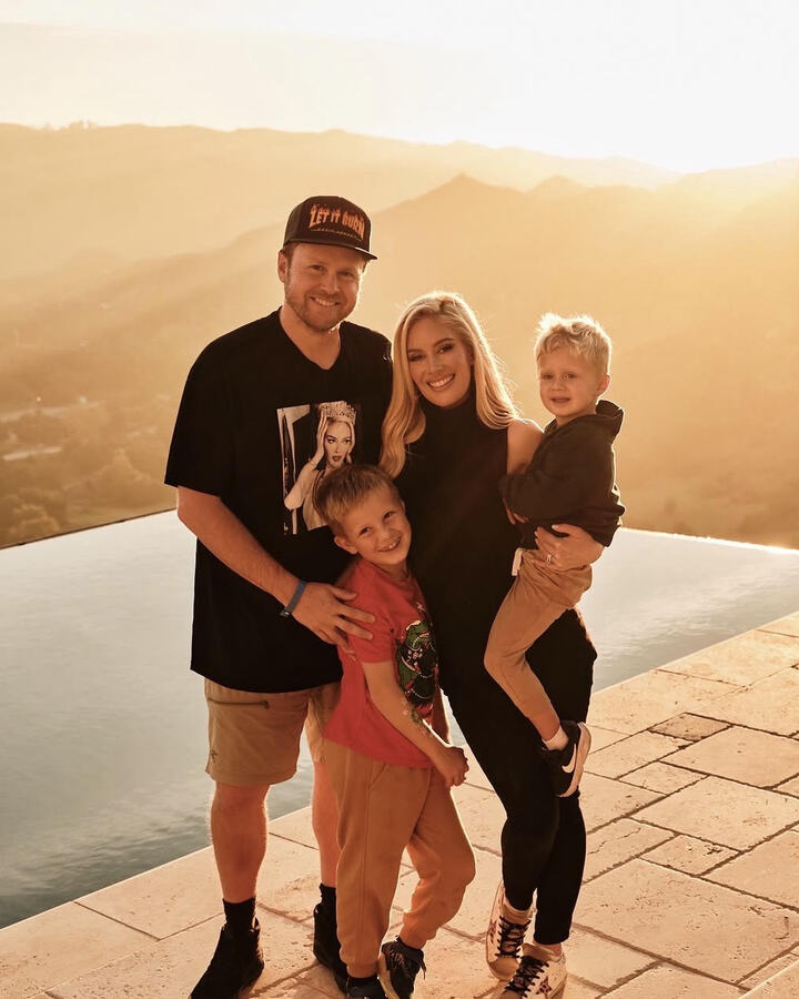 Heidi Montag, Spencer Pratt, and their two young sons stand together beside an infinity pool at golden hour, the hills glowing behind them.