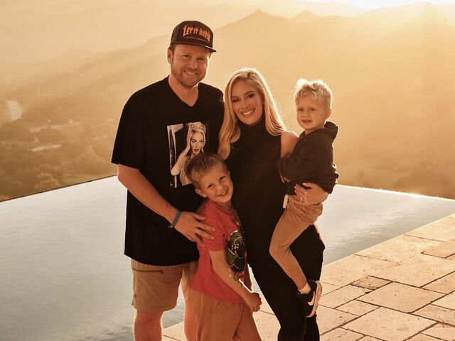 Heidi Montag, Spencer Pratt, and their two young sons stand together beside an infinity pool at golden hour, the hills glowing behind them.