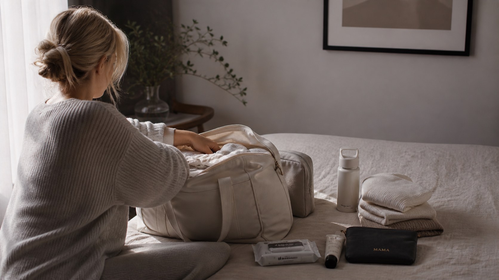 A woman packing a soft cream weekender bag on a bed.