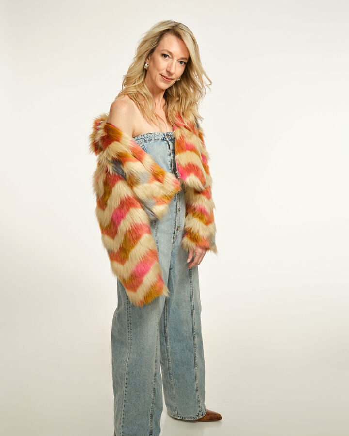 Julie Cole stands in wide-leg denim and a striped faux-fur coat slipped off one shoulder, against a soft white backdrop.