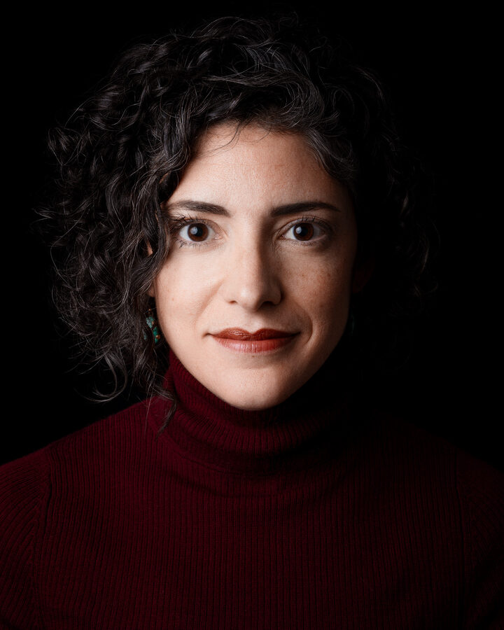 Julie Scelfo, in a deep red turtleneck with dark curly hair, photographed against a black background.