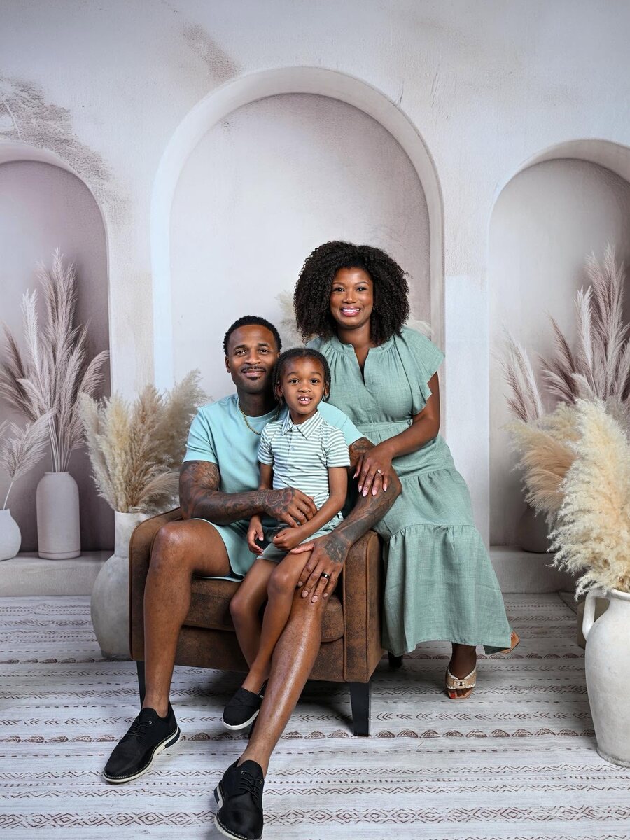 LaShonda Unseld Hopkins stands beside her husband, who holds their son Major on his lap, all three in matching sage green in a softly lit studio.