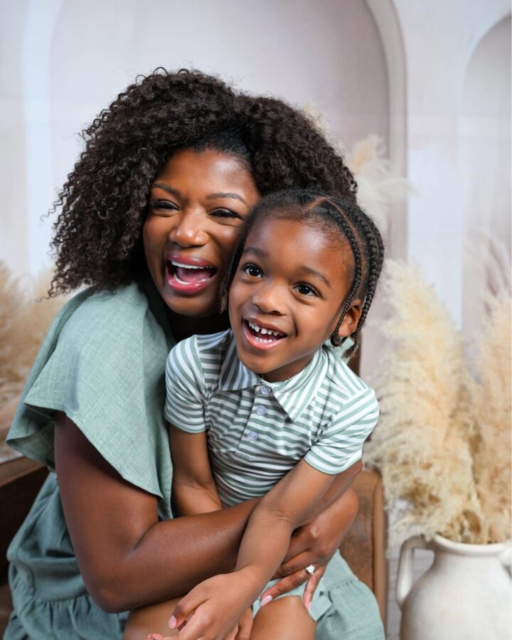 LaShonda Unseld Hopkins laughs with her arms wrapped around her young son Major, both in matching sage green against a soft arched backdrop.
