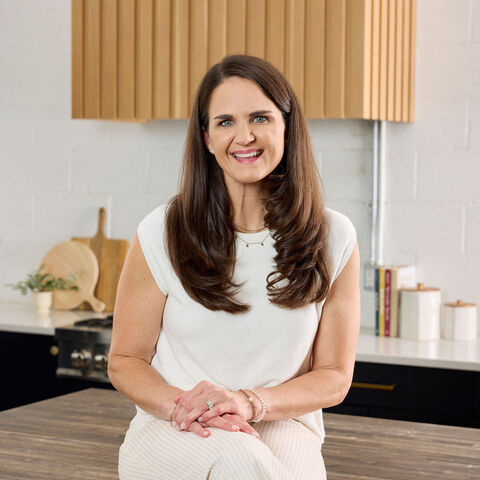Maegan Brown stands in her white kitchen with her four children around a mixing bowl of cookie dough, one son on the counter licking the paddle attachment.