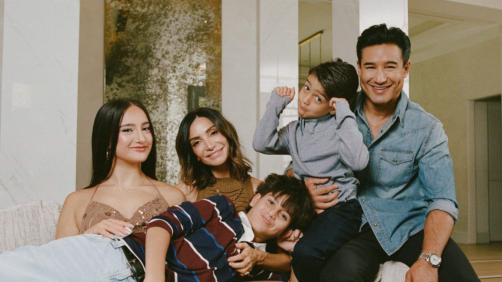 Mario and Courtney Lopez sit on a cream sofa with their three children, Gia lounging in a sequined dress, Nico sprawled across the cushions in a striped sweater, and Sonny flexing on his father&rsquo;s knee.