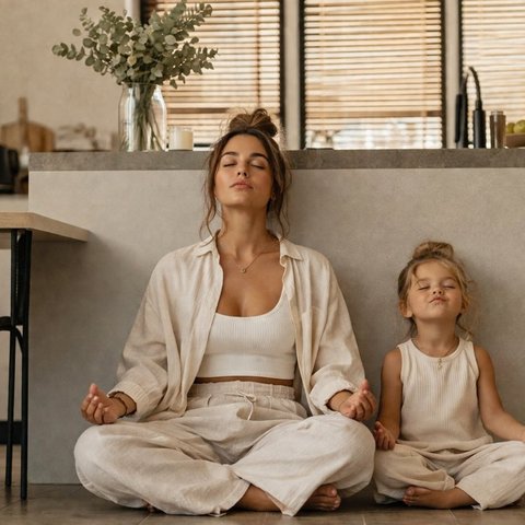 A mother and her young daughter meditating on the kitchen floor in soft morning light