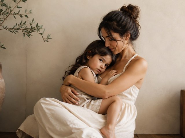 A mother holding a baby while looking at a cluttered kitchen counter.