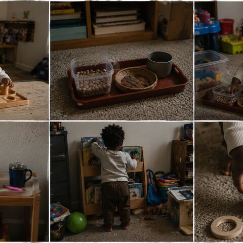 A toddler in a cream sweater works independently with simple wooden materials and trays on the floor and a low table in a lived-in home.