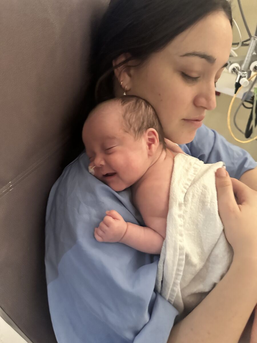 Rachel rests with Brooklyn held skin-to-skin against her chest in the NICU, both with their eyes closed.