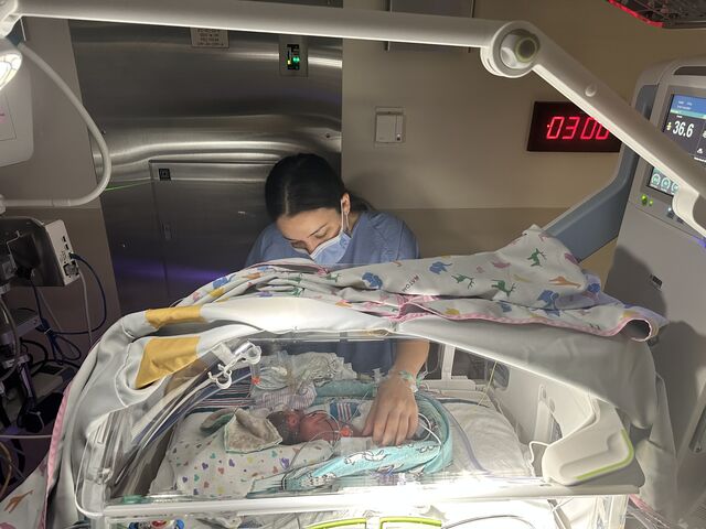 Rachel Abugov leans over an incubator in the NICU beside her newborn daughter.