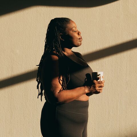 A woman sits alone on a sunlit porch step with a mug in her hands, looking out past the frame.