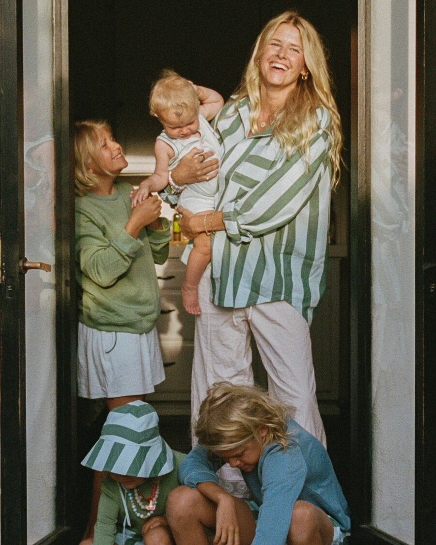 Sarah Wright Olsen laughs in the doorway of her white stucco home, her baby on one hip and her three older children around her in green and blue stripes, the family dog stretched out on the step.