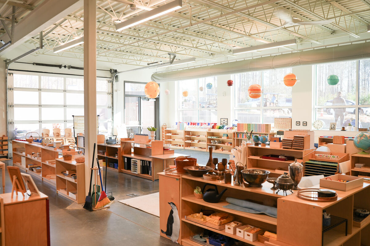 A bright classroom at Terra School with low wooden shelves of learning materials, paper planets hanging from the ceiling, and windows opening onto the trees outside.