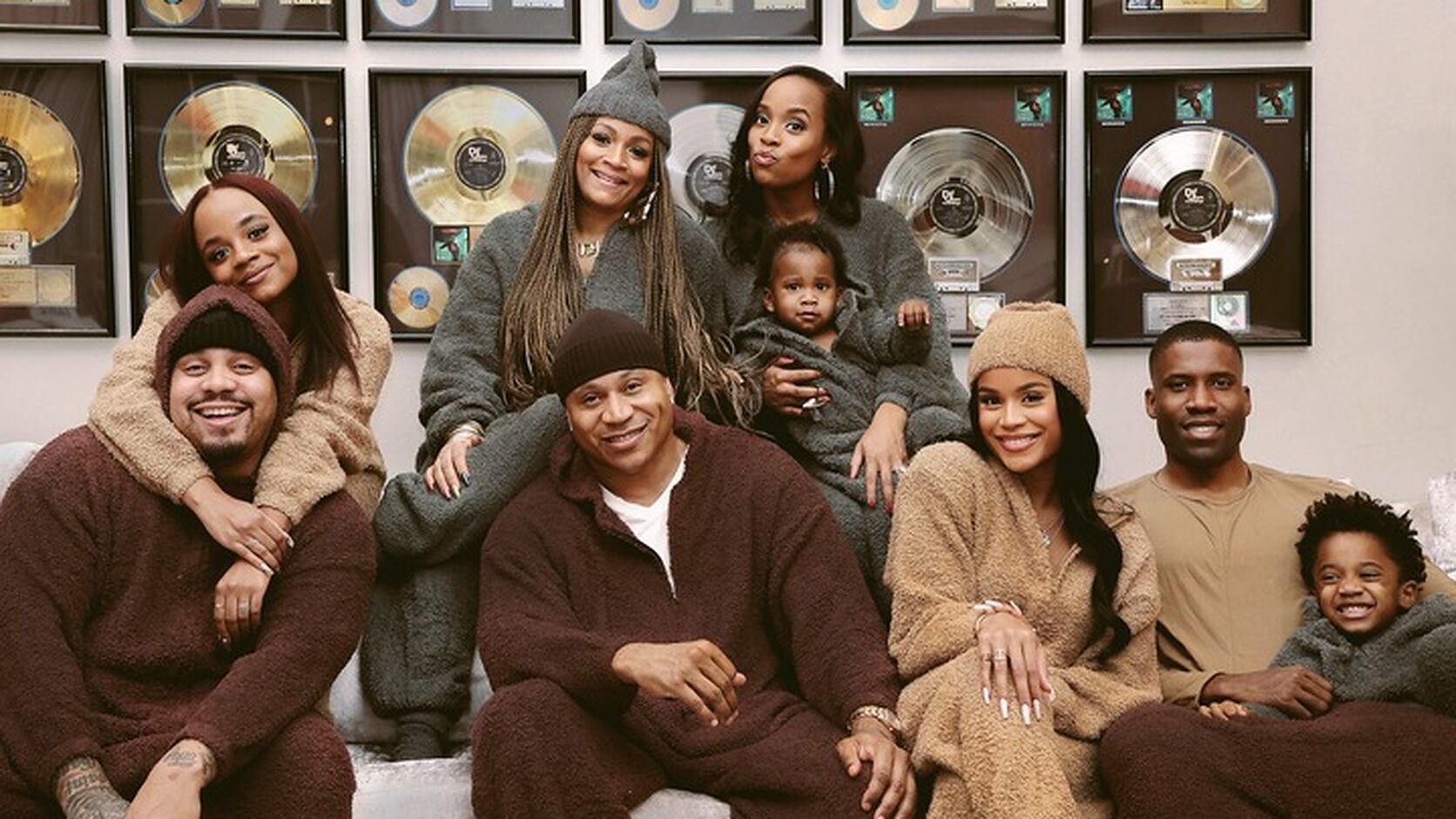 Simone I. Smith sits at the centre of her family in matching brown and grey loungewear, in front of a wall of framed gold and platinum records.