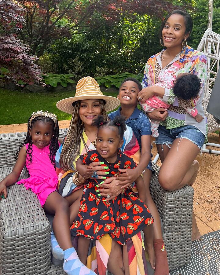 Simone I. Smith sits at the centre of her family in matching brown and grey loungewear, in front of a wall of framed gold and platinum records.