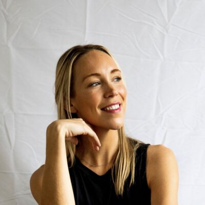 Headshot of Blair West, a Momé contributor, smiling with her hand resting near her chin against a white backdrop.