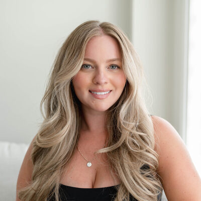 Headshot of Brittany Krystantos, a Momé founder and editor, with long blonde hair and a black top, smiling on a white sofa.