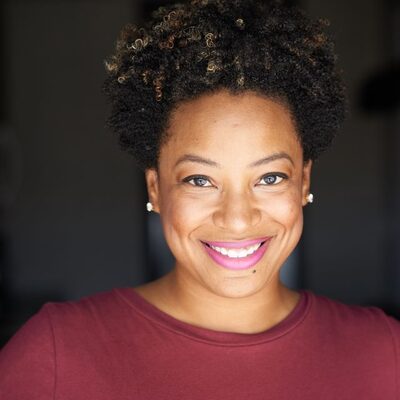 Headshot of Leah Frazier, a Momé contributor, smiling in a maroon top against a dark background.