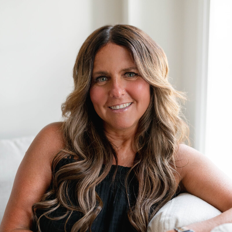 Headshot of Mandy Krystantos, a Momé contributor, smiling on a sofa in a black top.