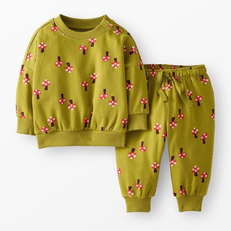 A Hanna Andersson baby sweatshirt and jogger set in olive green, printed all over with small red-and-white mushrooms, laid flat side by side.