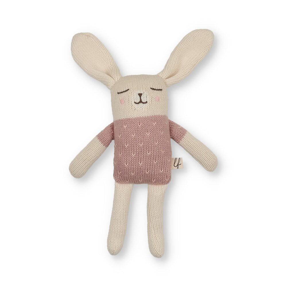A knitted bunny doll with long cream ears, a sleepy stitched face and rosy cheeks, wearing a dusty-pink textured knit top over cream legs.