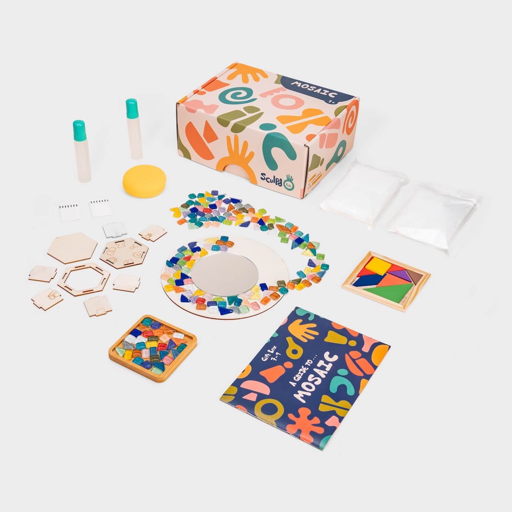 The Sculpd Kids Mosaic Kit laid out flat: a patterned gift box, coloured glass mosaic tiles, a round mirror part-tiled, wooden pot pieces, glue, grout pouches and an illustrated mosaic guide.