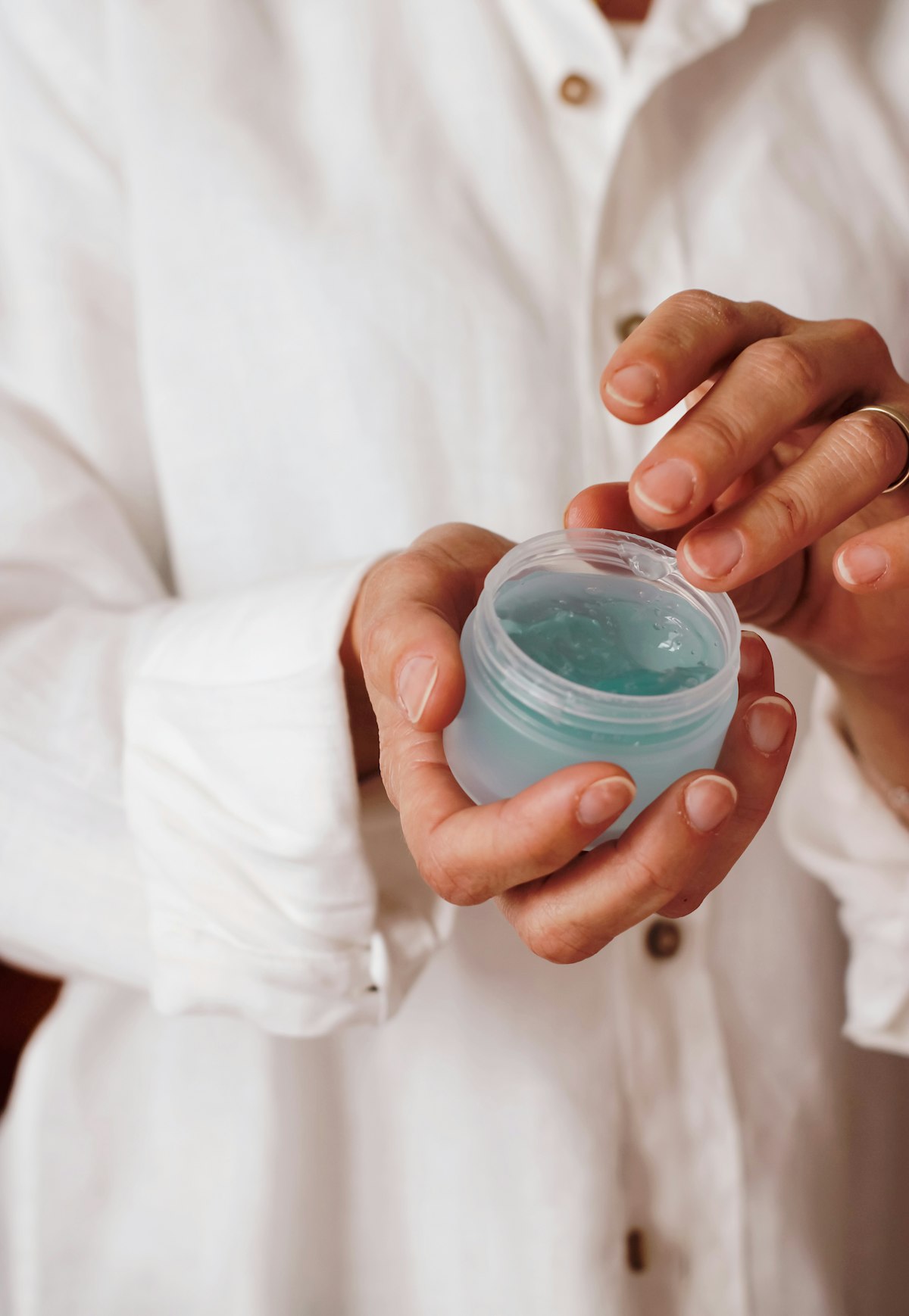 Hands holding a small jar of organic Earth Mama nipple butter against a soft cream sweater.