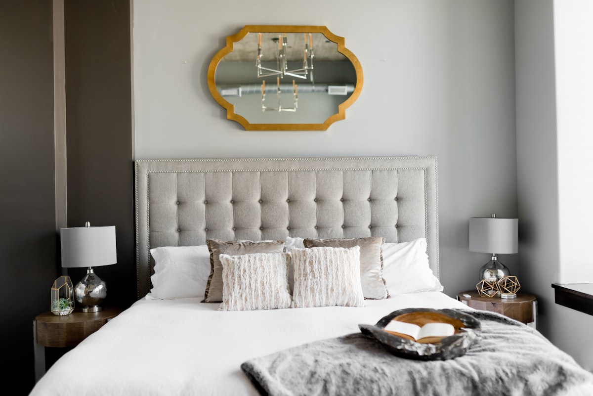 A made bed with cream linens and a brass mirror, soft morning light, neutral interiors