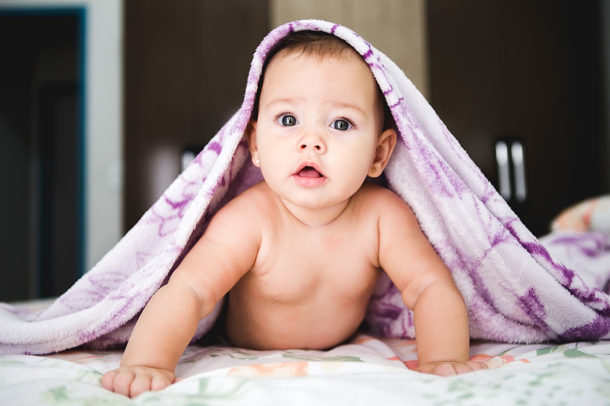 A baby tucked under a warm purple blanket, looking up curiously