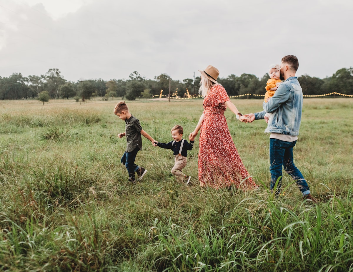 A family of five walking through a sunlit field.
